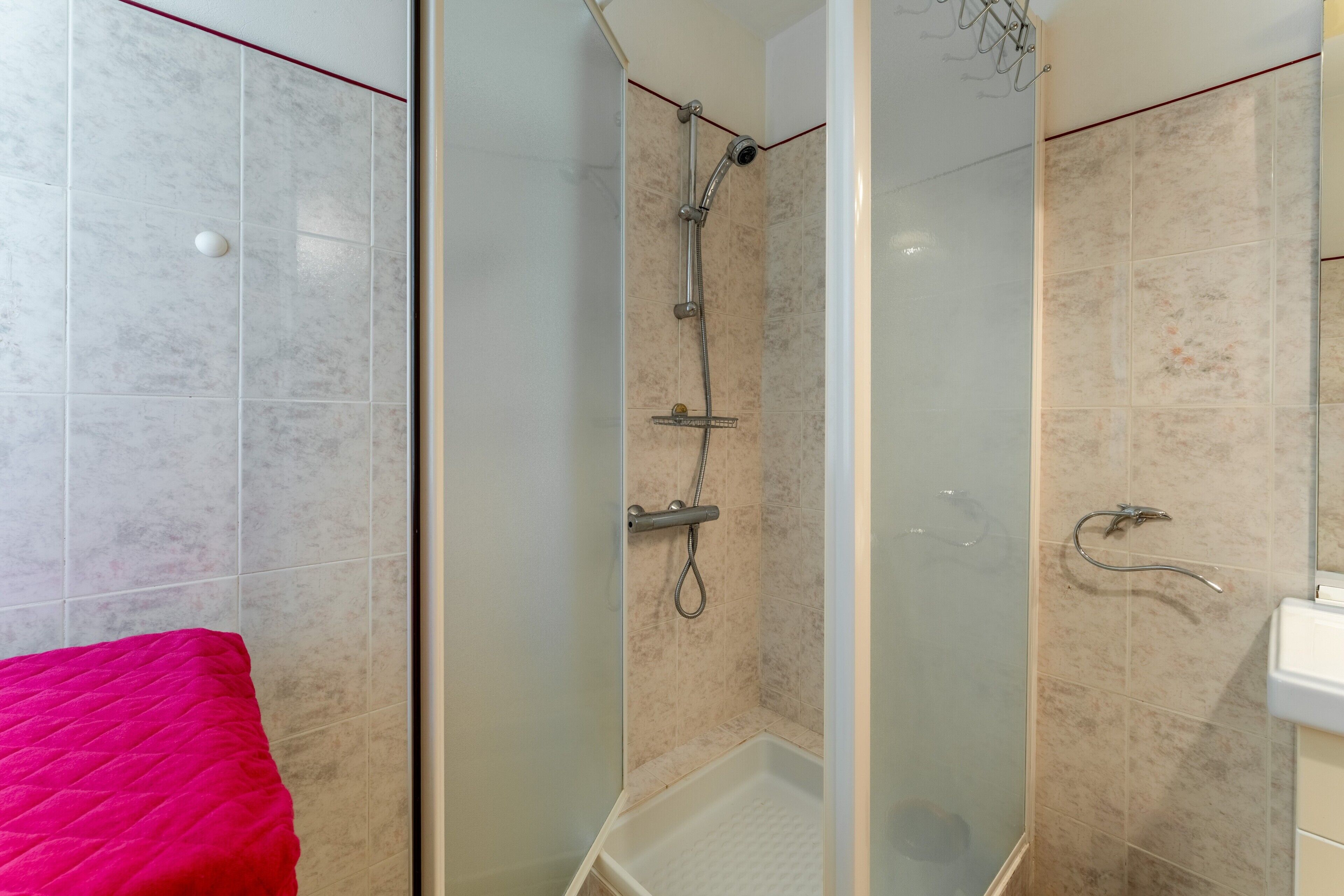 Une douche avec une porte en verre, un lavabo blanc et une serviette rouge.