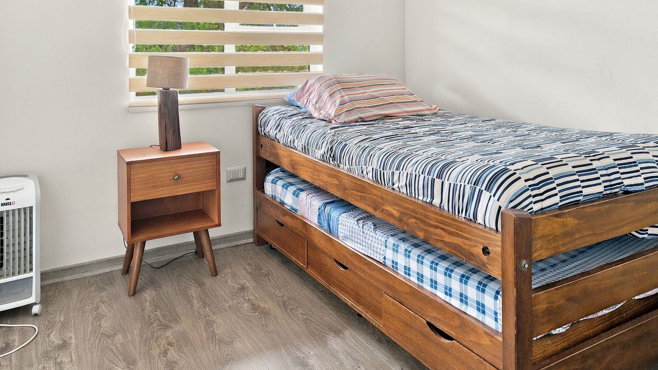 A compact bedroom with a wooden bunk bed, a bedside table, and a radiator.