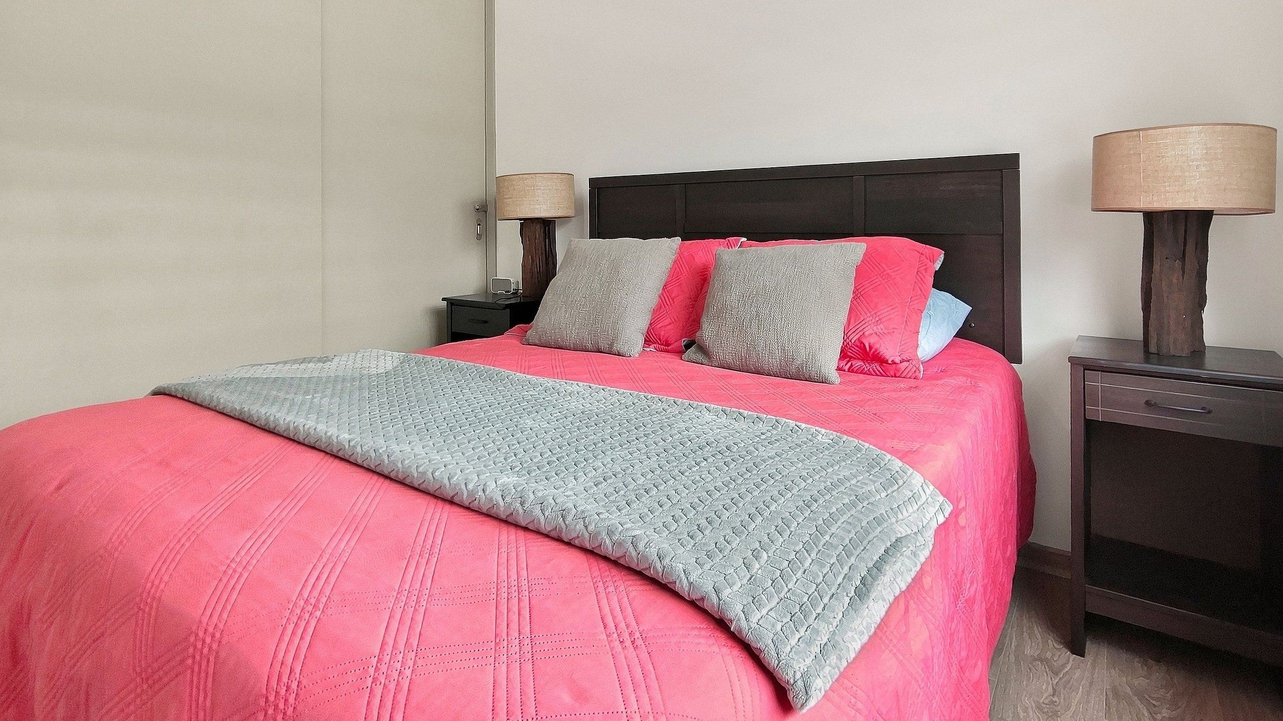 A bed with a pink and grey quilt, two bedside tables with lamps, and a wooden headboard.