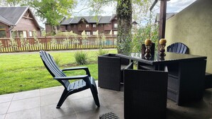 A patio with a chair and wicker furniture, a wooden fence, and houses in the background. - Oceana Suites Los Nostros (Pucon)