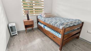 A small, single-bed room with a wooden bed, a bedside table, a lamp, and a heater.