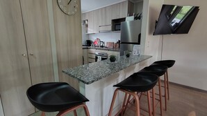 A kitchen with a granite countertop, stainless steel appliances, and a flat-screen TV mounted on the wall. - Oceana Suites Los Nostros (Pucon)