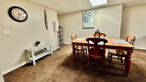A dining area with a wooden table, four chairs, a white bench, a clock, a bookshelf, and a skylight. - Beautiful Suite with Fenced yard + in suite Kitchen and Laundry (St. Albert)