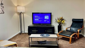 A hotel room with a bed, a television on a stand, a desk with a lamp, a chair, and a vase with flowers. - Beautiful Suite with Fenced yard + in suite Kitchen and Laundry (St. Albert)