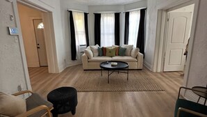 Un salon spacieux avec un canapé beige, une table basse et un pouf noir.
