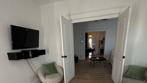 Une chambre spacieuse avec un grand lit, un téléviseur fixé au mur et un coin salon avec des fauteuils.