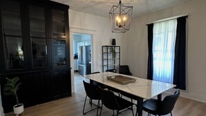 Un vaste espace dédié à la salle à manger, avec une grande table et des chaises, un luminaire suspendu, et une vue sur la cuisine et le salon.