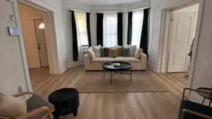 Un salon spacieux avec un canapé beige, une table basse et un pouf noir.