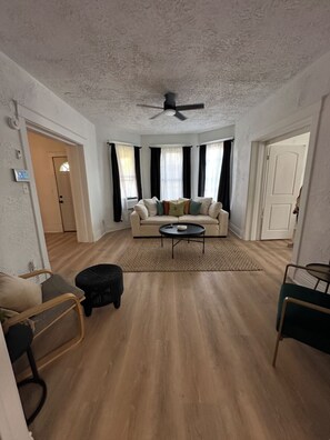 Ein geräumiges Wohnzimmer mit einem beigefarbenen Sofa, einem Couchtisch und einem schwarzen Ottomanen.