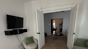 Une chambre spacieuse avec un grand lit, un téléviseur fixé au mur et un coin salon avec des fauteuils.