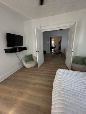 Ein geräumiges Zimmer mit einem großen Bett, einem an der Wand montierten Fernseher und einer Sitzecke mit Stühlen.