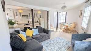 A modern living room with a grey sectional sofa, a blue patterned rug, and a dining area with wooden chairs.