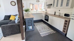 A compact kitchen with white cabinets, a built-in oven, and a microwave. There's a grey sofa with yellow cushions in the adjacent living area.