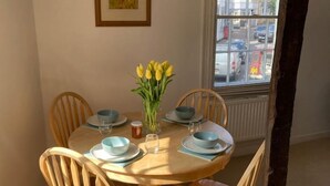 A round wooden dining table with blue plates and bowls, surrounded by wooden chairs. A vase with yellow flowers is on the table.