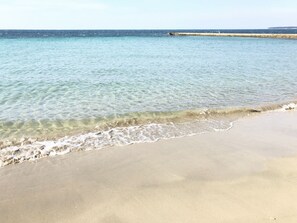 A beach with clear water, a sandy shore, and a distant pier.