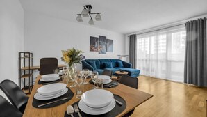 Ein modernes Wohnzimmer mit Essbereich, einem blauen Sofa und einem großen Fenster mit Vorhängen.