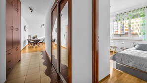 Ein modernes Schlafzimmer mit Bett, einem Fenster mit grünen Vorhängen sowie einem Essbereich mit Tisch und Stühlen.
