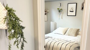 Quarto com cama, planta pendente e quadro na parede.
