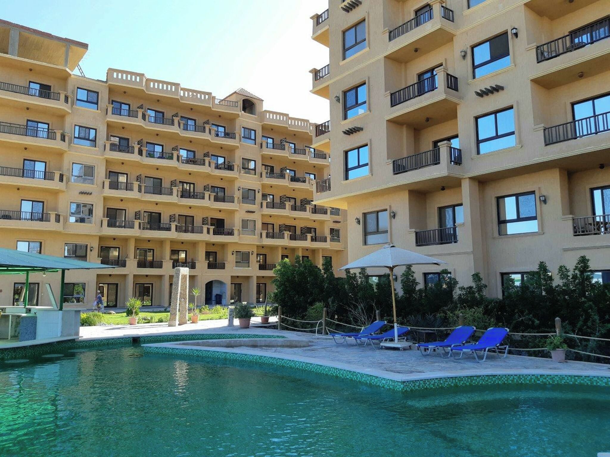 A multi-story hotel with balconies, a swimming pool, and lounge chairs.