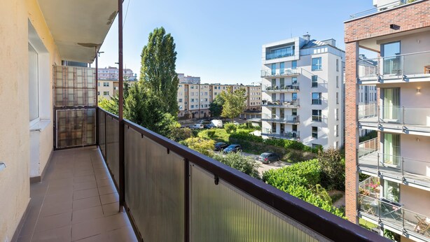Un balcón con vista a una zona residencial, que incluye edificios de varios pisos y coches aparcados.