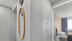 Un dormitorio moderno con un espejo grande, una cama con cabecera gris y una mesita de noche con lámpara.