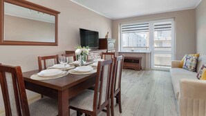 Un comedor con una mesa de madera dispuesta para cuatro personas, un televisor y una ventana con persianas.