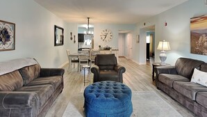 A spacious living room with leather sofas, a blue ottoman, and a dining area with a chandelier. - Prime Pines | Great Views, Great Location, Resort Amenities (Pigeon Forge)