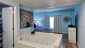 A bathroom with a large bathtub, a door, and a wall with a floral painting. - Prime Pines | Great Views, Great Location, Resort Amenities (Pigeon Forge)