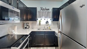 A modern kitchen with dark cabinets, stainless steel appliances, and a window with a view. - Prime Pines | Great Views, Great Location, Resort Amenities (Pigeon Forge)