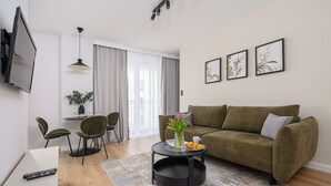 A modern living room with a green sofa, a round coffee table, and a dining area with a table and chairs. - P&O Apartments PORY (Warsaw)