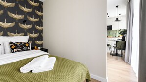 A hotel room with a bed, a green textured bedspread, a patterned wall, a dining area with a table and chairs, and a modern pendant light. - P&O Apartments PORY (Warsaw)