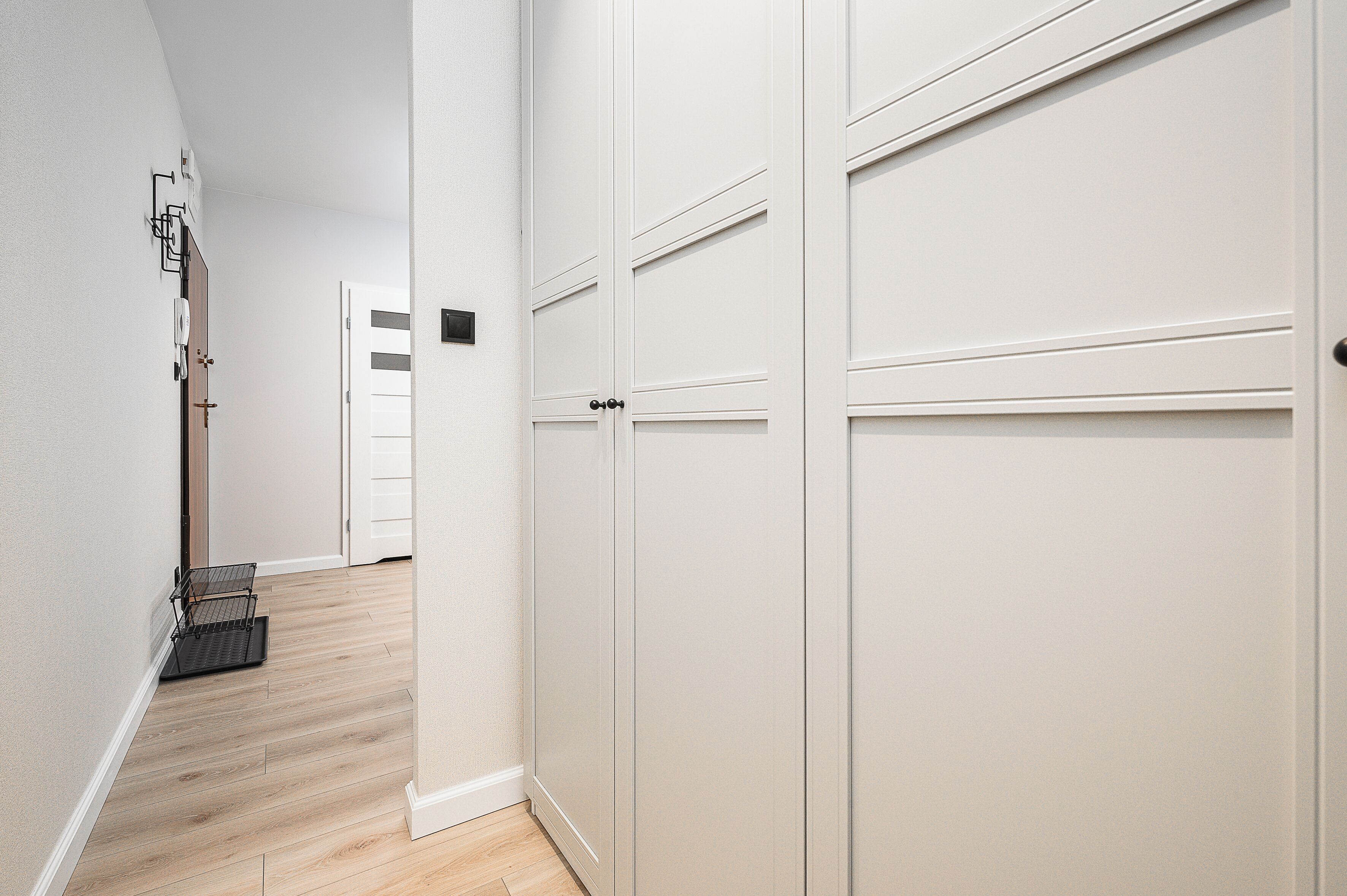 Un couloir avec un plancher en bois, des murs blancs et une porte fermée.