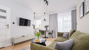 A modern living room with a green sofa, a small round table with a vase of flowers, and a flat-screen TV mounted on the wall. - P&O Apartments PORY (Warsaw)