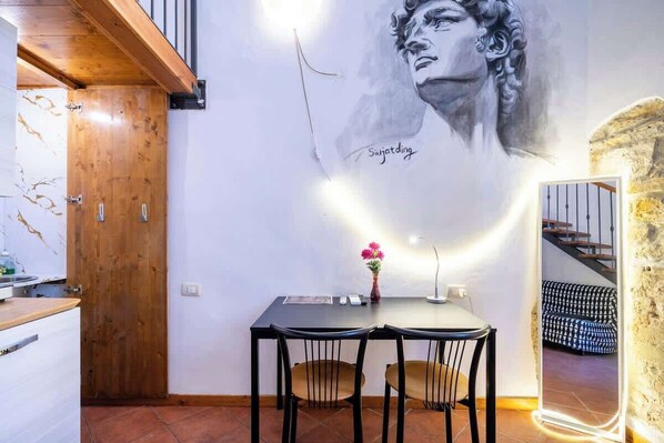 A dining area with a table and chairs, a vase with flowers, and a wall mural.