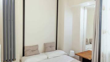 Ein modernes Hotelzimmer mit einem großen Bett, einem Nachttisch, einer Lampe, einem Spiegel und einem Fenster mit Vorhängen.