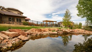 A residential area with a pond, a wooden pergola, and a house with a fenced patio.