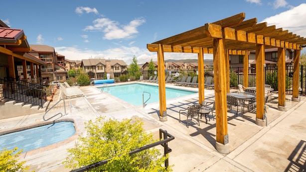 A pool area with a wooden pergola, lounge chairs, and a swimming pool.