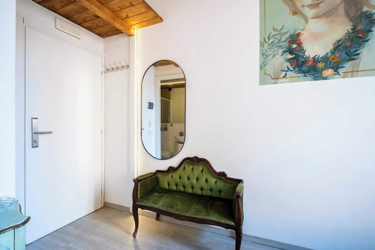 Une pièce avec un banc recouvert d’un tissu vert, une porte blanche et un miroir au mur.