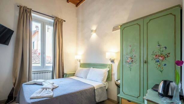 A bedroom with a bed, a wardrobe, a desk, and a window with curtains. - Duomo Studio Room with Private Bath and Kitchenette (Firenze)