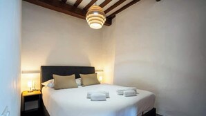 Cama bem arrumada com lençóis brancos e duas almofadas, abajur e luminária pendente moderna.