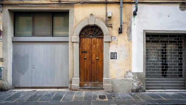 Um edifício com porta de madeira, porta de garagem e rua com calçada de pedra.