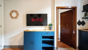 Uma cozinha moderna com armário azul, TV fixada na parede exibindo o logotipo da Netflix e porta de madeira que dá para outro cômodo.