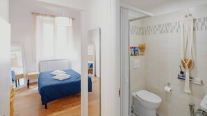 Une chambre d’hôtel avec un lit, une salle de bain avec douche et un petit coin salon.