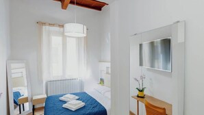Une chambre à coucher comprenant un lit, un bureau, une chaise, un miroir, une fenêtre avec des rideaux et un radiateur.