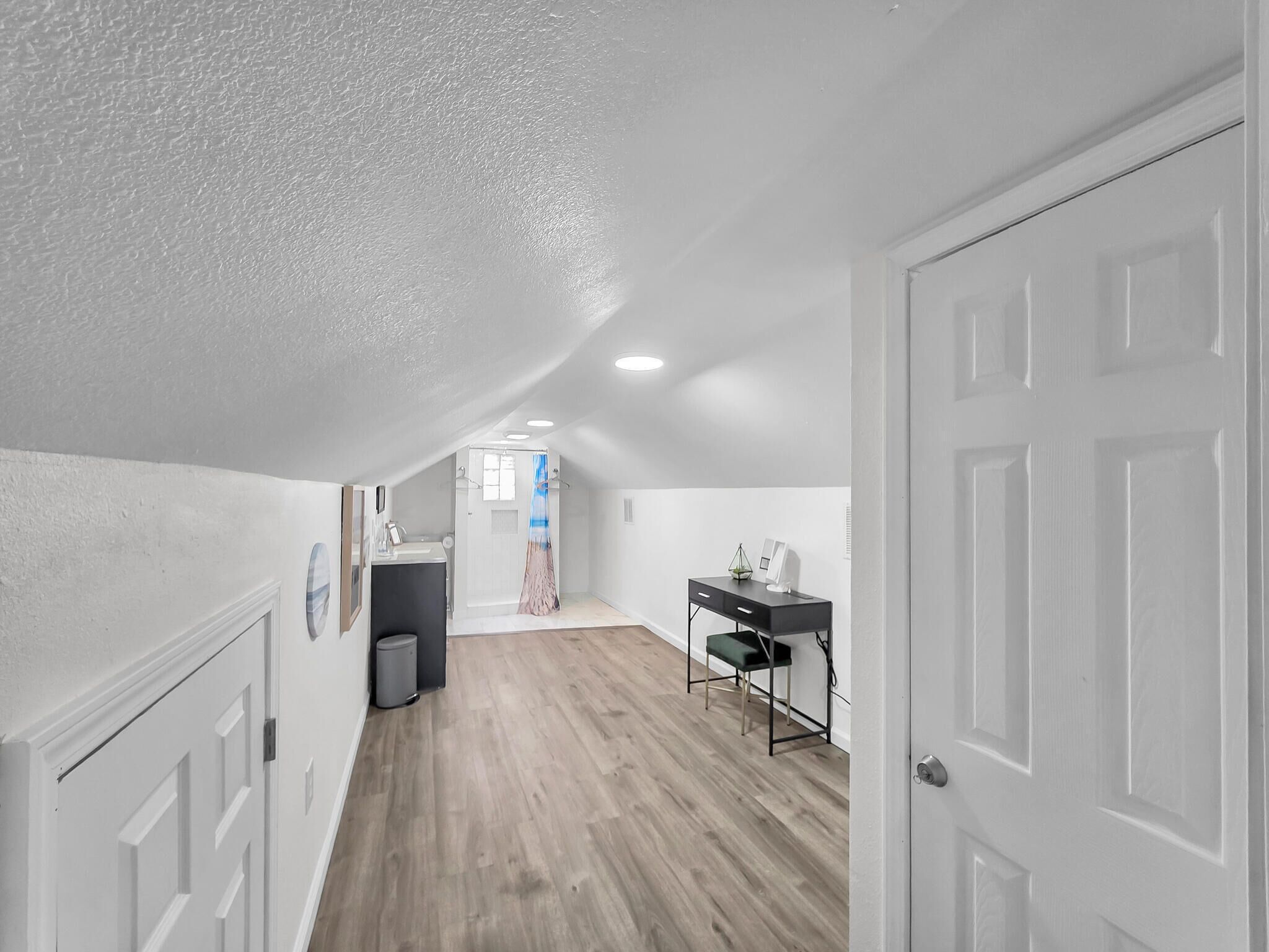 Un couloir étroit avec un plancher en bois, des murs blancs et une porte sur le côté droit.