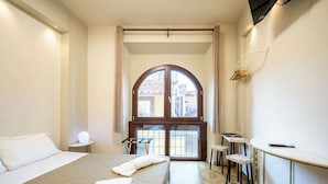 A hotel room with a large bed, a small table, two chairs, a desk, and a large window with a view of buildings. - Duomo Room with Private Bath, WiFi and Netflix (Firenze)
