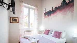 A bedroom with a bed, a window with curtains, a wall painting, and a framed picture. - Private Duomo Room with Ensuite Bath (Firenze)