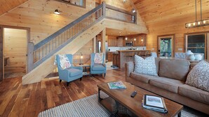 A spacious living area with a wooden staircase, a kitchen in the background, and a large window. - Morning Glory - Cherry Log GA (Cherry Log)