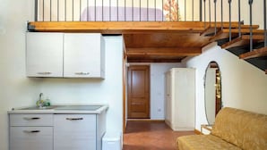 Een compacte keuken met witte kasten, een spoelbak en een klein aanrecht. Er is een houten trap met een metalen leuning die naar een hoger gelegen niveau leidt.
