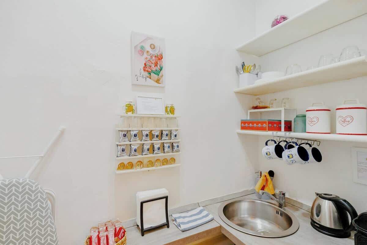 A kitchen with white shelves, a stainless steel sink, and a kettle.
